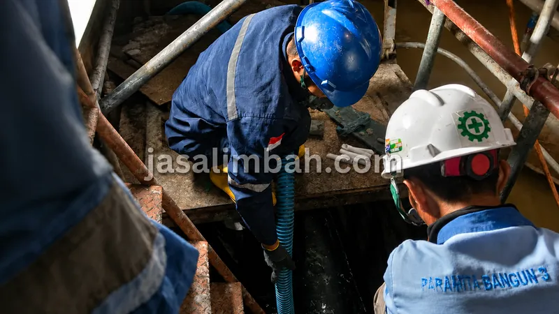 Teknisi Jasa Limbah bekerja sama menyedot limbah di ruang sempit pabrik