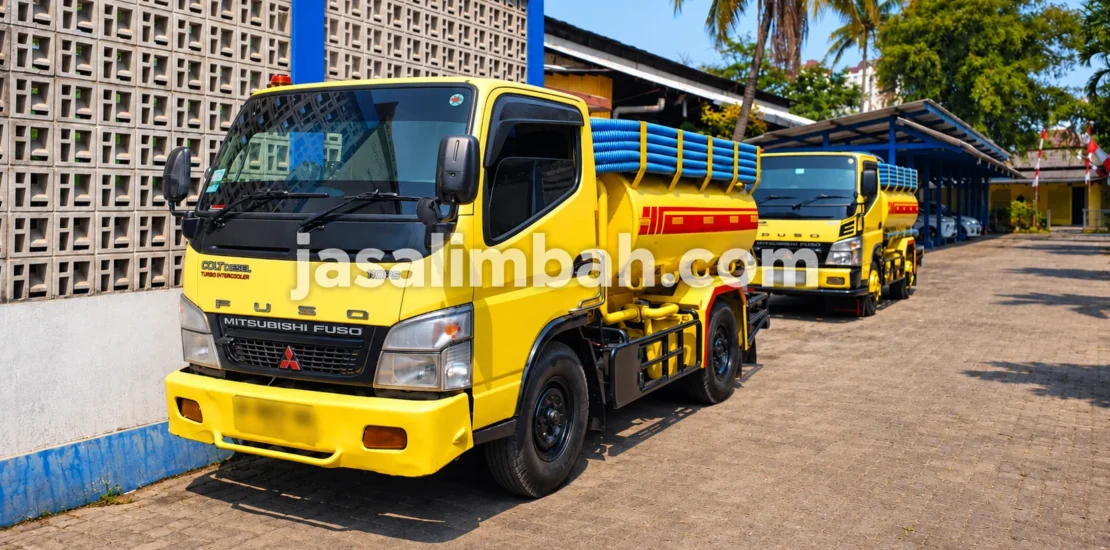 Truk sedot limbah JasaLimbah.com berwarna kuning dengan selang vakum di area operasional
