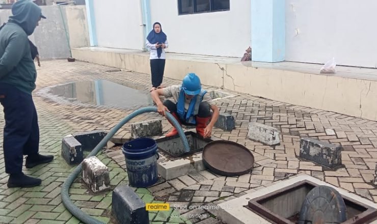 Petugas sedot WC melakukan penyedotan septic tank menggunakan selang vakum di area perkantoran