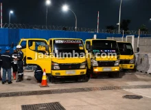 Tiga truk sedot limbah Mitsubishi Fuso berwarna kuning terparkir di area industri pada malam hari.