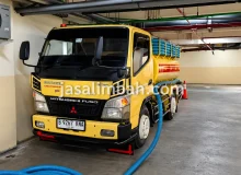 Truk sedot limbah cair Mitsubishi Fuso Colt Diesel terparkir di basement gedung dengan selang biru terpasang
